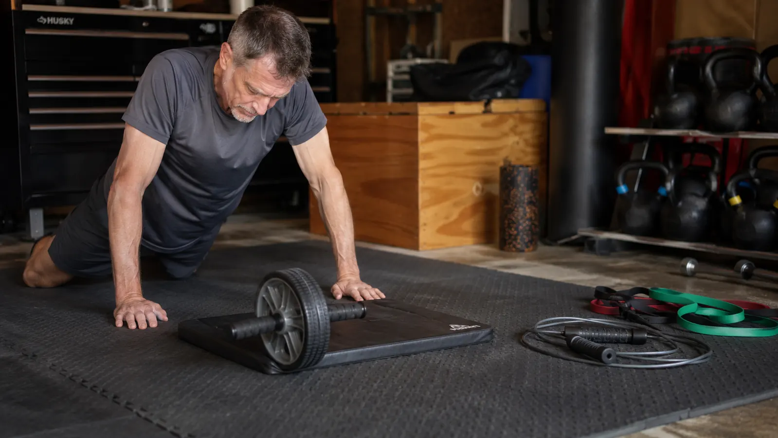 The wheel and knee mat centered on a workout floor, the jump rope and band handles placed off to one side out of use.